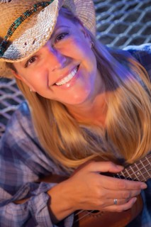 Beautiful evening portrait of cowgirl near campfire playing her ukulele