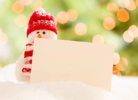 Cute snowman with scarf and hat next to blank white card over abstract background