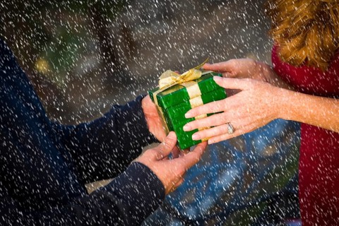 Hands of man and woman exchanging a wrapped christmas gift in the snow