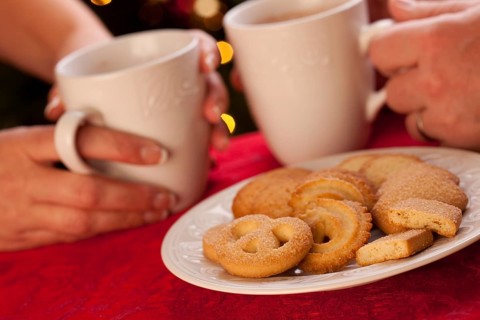 Man and woman sharing hot chocolate and cookies in front of holiday lights