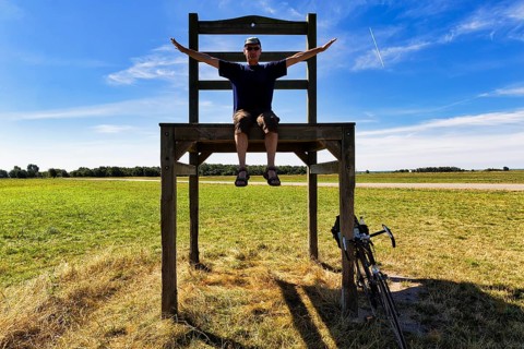 Cyclist sits on oversized chair in a meadow
