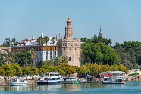 View over the river Rio Guadalquivir on promenade with excursion boats and Torre del Oro