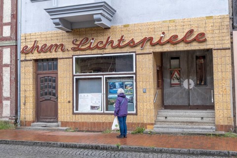 A woman stands in front of the shop window of the former cinema in Doemitz