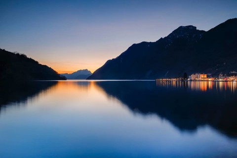 Illuminated lakeside promenade of Brunnen and view over Lake Lucerne at sunset with Mount Pilatus in the background