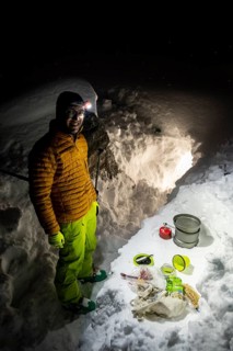 Man cooking with a camping stove in front of a snow cave
