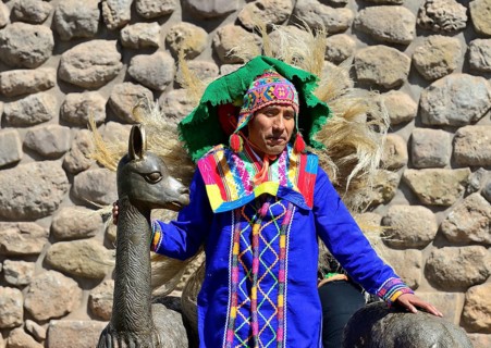 Indigenous man in colorful traditional costume in front of an Inca wall