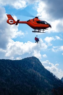 Two flight rescuers of the Bavarian Mountain Rescue Service hang on the wire rope of the rescue helicopter Christoph 14