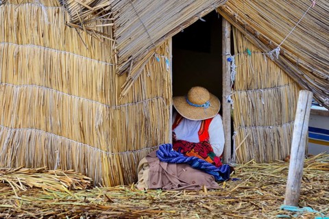 Indigenous woman embroidering in front of the reed hut on a Uro floating island