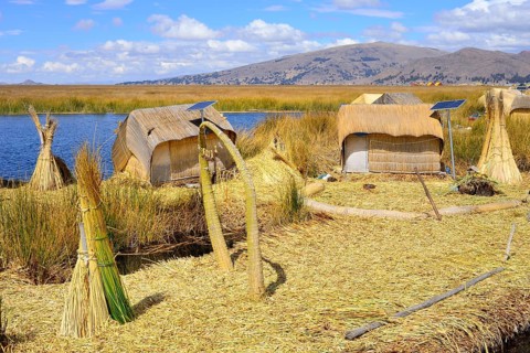 Reed bundles in front of reed huts with solar cells on a floating island of the Uro