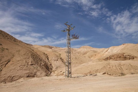 High-voltage pylon in front of mountain range with blue sky in Negev desert