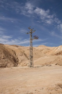 High-voltage pylon in front of mountain range with blue sky in Negev desert