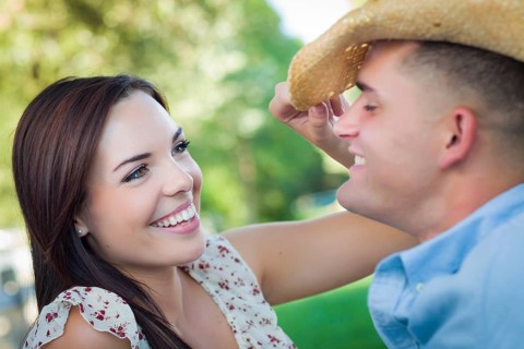Happy mixed-race romantic couple with cowboy hat flirting in the park