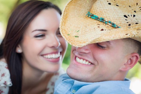 Happy mixed-race romantic couple with cowboy hat flirting in the park