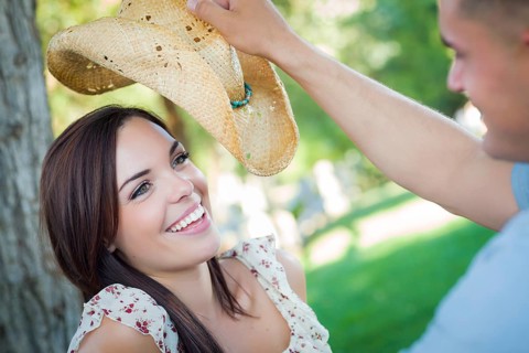 Happy mixed-race romantic couple with cowboy hat flirting in the park