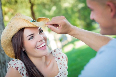 Happy mixed-race romantic couple with cowboy hat flirting in the park