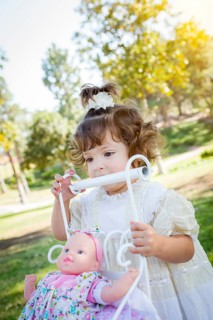 Adorable young baby girl playing with her baby doll and carriage outdoors