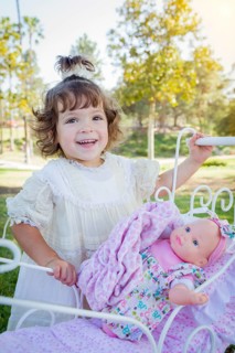 Adorable young baby girl playing with her baby doll and carriage outdoors