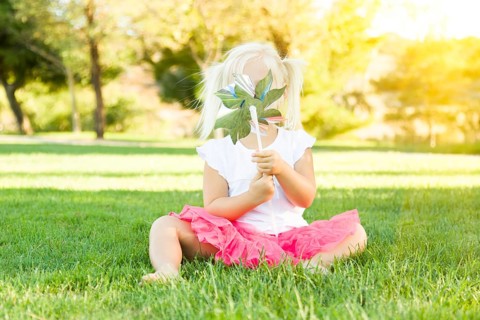 Cute little girl sitting in grass blowing on pinwheel toy
