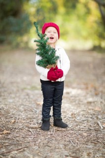 Baby girl in red mittens and cap holding small christmas tree outdoors