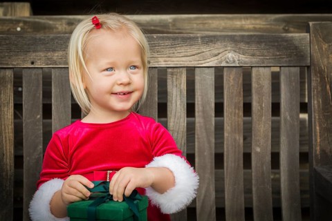 Adorable little girl unwrapping her gift on a bench outside
