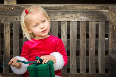 Adorable little girl unwrapping her gift on a bench outside