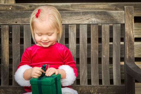 Adorable little girl unwrapping her gift on a bench outside