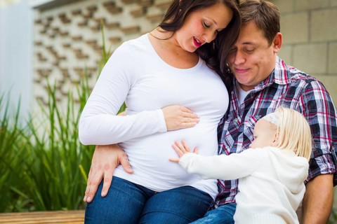 Adorable baby girl puts her hand on stomach of mommy as daddy looks on