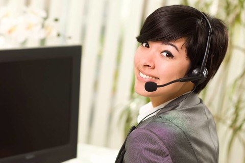 Attractive young woman smiles wearing headset near her computer monitor