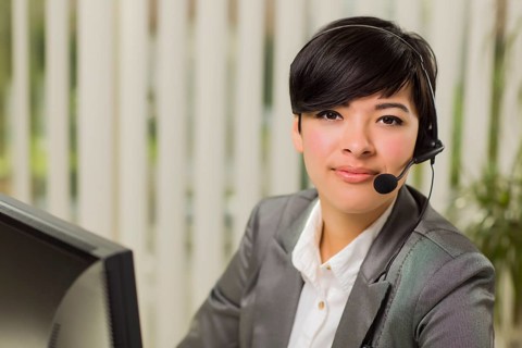 Attractive young mixed-race woman smiles wearing headset near computer monitor