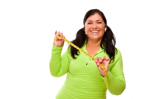 Attractive middle aged hispanic woman in workout clothes showing off her tape measure against a white background