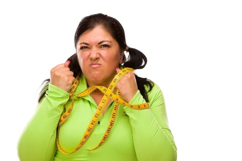 Attractive frustrated hispanic woman tied up with tape measure against a white background