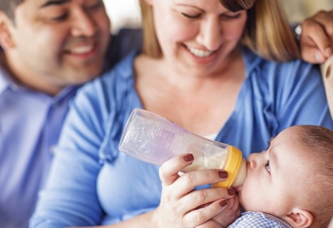 Happy attractive mixed-race couple bottle feeding their son