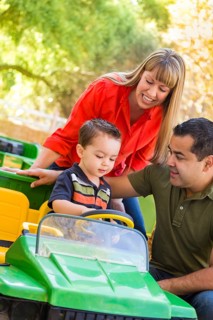 Happy young mixed-race boy enjoys A toy tractor while parents look on