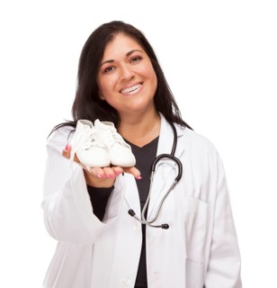 Attractive hispanic female doctor or nurse holding out baby shoes isolated on a white background
