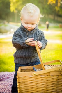 Adorable little blonde baby boy opening a picnic basket outdoors at the park