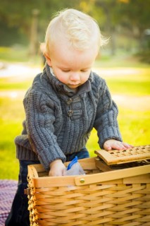 Adorable little blonde baby boy opening a picnic basket outdoors at the park