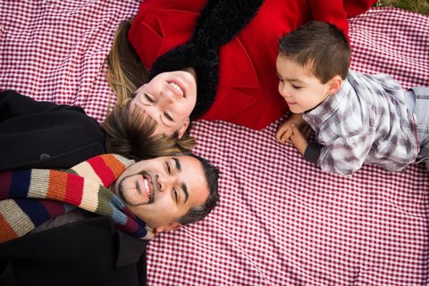 Young mixed-race family in winter clothing laying on their backs on picnic blanket in the park together