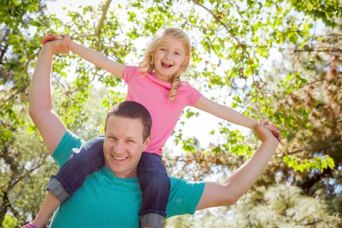 Cute young girl rides piggyback on her dads shoulders outside at the park
