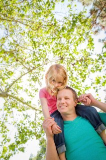 Cute young girl rides piggyback on her dads shoulders outside at the park