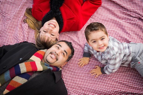 Young mixed-race family in winter clothing laying on their backs on picnic blanket in the park together