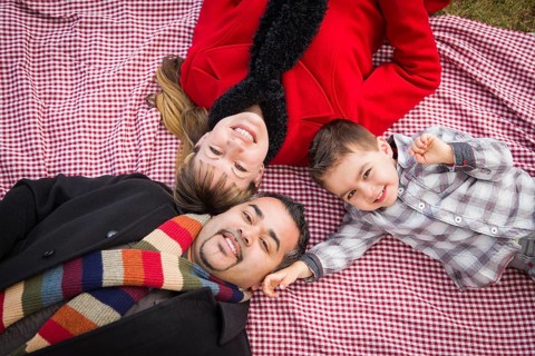 Young mixed-race family in winter clothing laying on their backs on picnic blanket in the park together