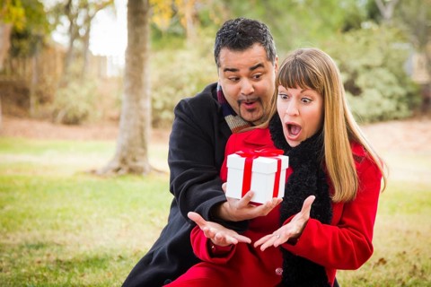 Young attractive mixed-race couple sharing christmas or valentines day gift in the park
