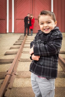 Young adorable mixed-race boy at train depot with parents smiling behind