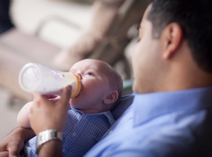 Happy hispanic father bottle feeding his very content mixed-race son