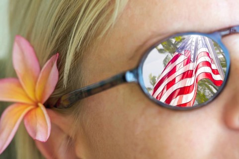 Girl with plumeria flower in hair and wearing sunglasses with reflection of american flag and palm trees