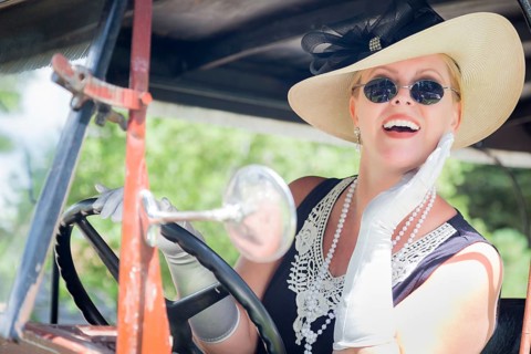Attractive young woman in twenties outfit driving an antique automobile