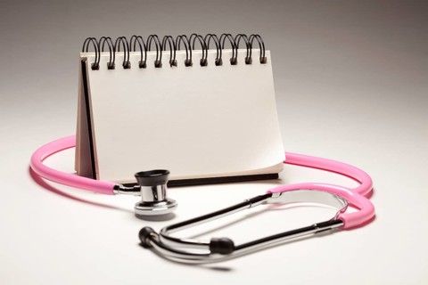 Blank spiral note pad and pink pediatric stethoscope on gradated background