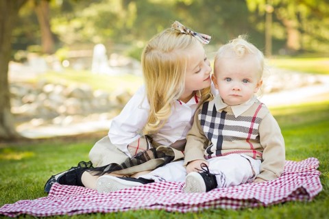 Sweet little girl kisses her baby brother on his cheek outdoors at the park