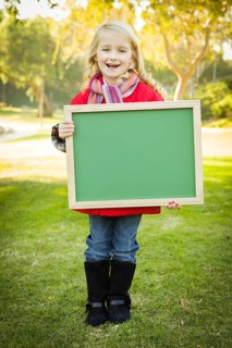 Cute little blonde wearing winter coat and scarf holding a green chalkboard outdoors