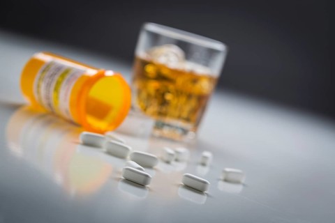Several prescription drugs spilled from fallen bottle near glass of alcohol